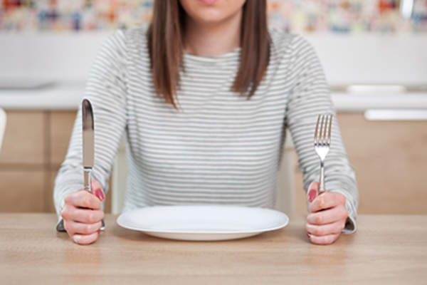 Woman holding up fork and knife next to an empty plate.