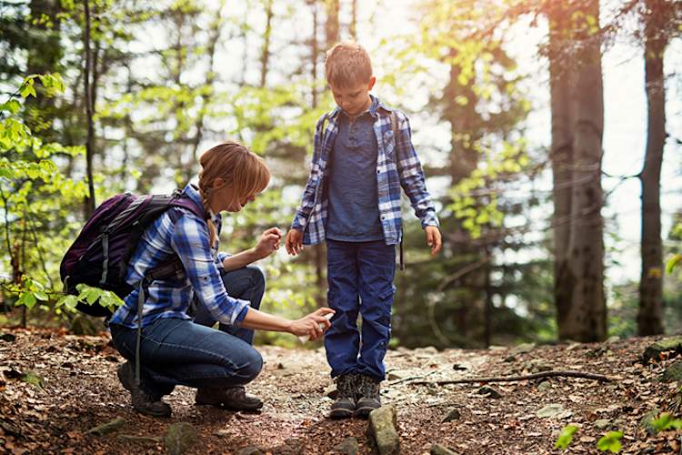 Mother putting insect spray on son on hike in woods.