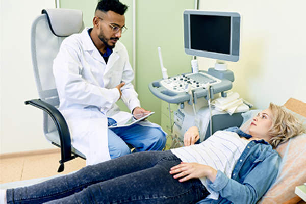 Doctor talking to patient lying on exam table about her adominal pain.