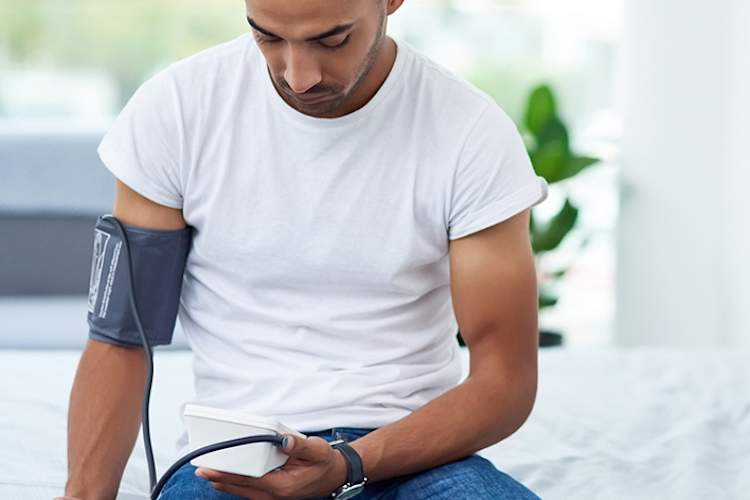 Young man measuring blood pressure sitting on bed at home.