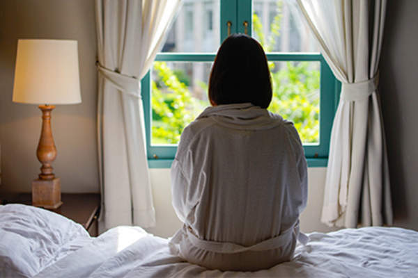 Woman feeling down sitting on her bed in her bathrobe.