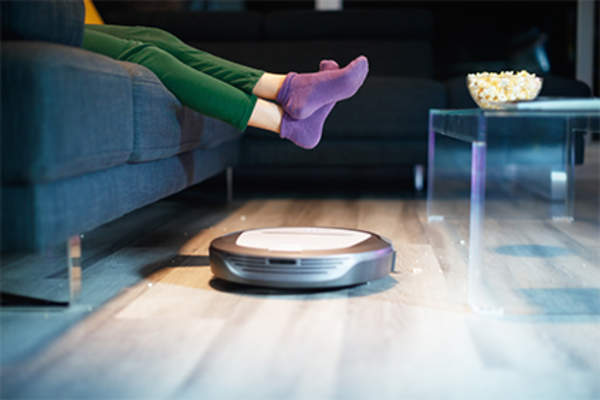 Robot vacuum, person watching television raising their feet.