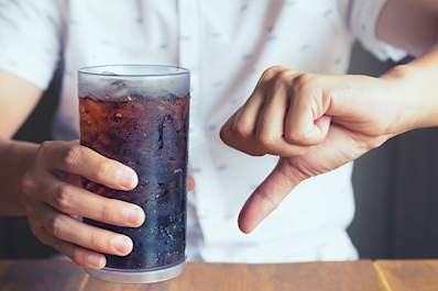 Man holding a glass of soda with a thumb-down.