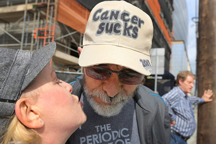 Jeffrey Weiss wears a hat that says “Cancer Sucks” as his wife kisses him