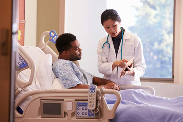 Doctor talking to man in hospital bed.
