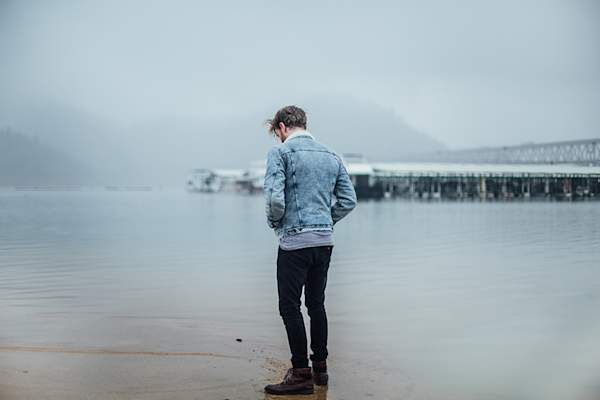 Depressed man standing on shore in winter