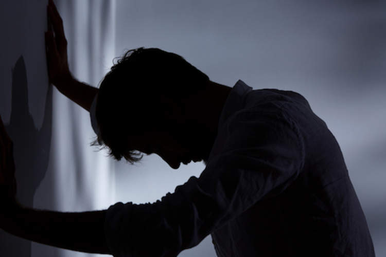 Crushing anxiety, man head down leaning against wall.
