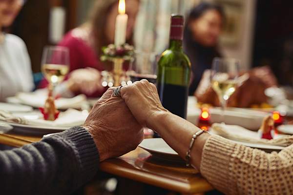 Family holding hands around a Thanksgiving dinner table.