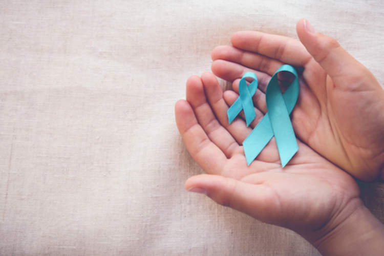 Hands holding two teal cancer awareness ribbons.