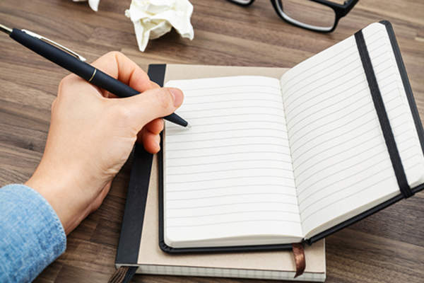 Left-handed person writing in a notebook.