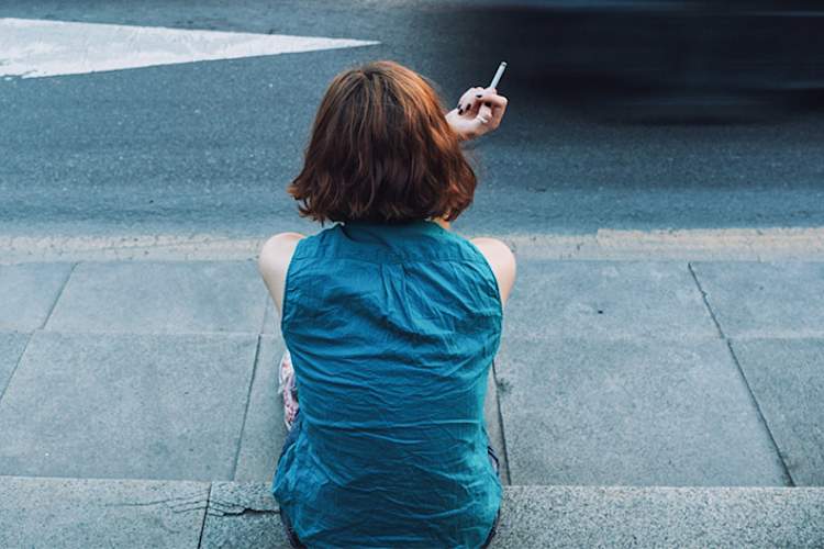 Young woman sitting outside on the steps smoking.