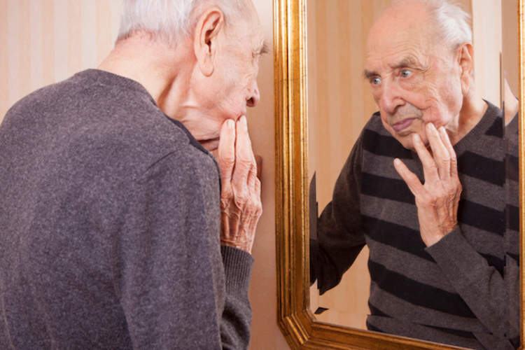 older man looking at face in mirror