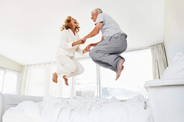 Adult couple laughing and jumping on bed at home.