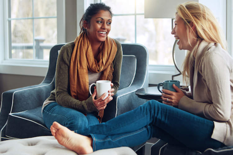 Two friends laughing and conversing, over coffee.