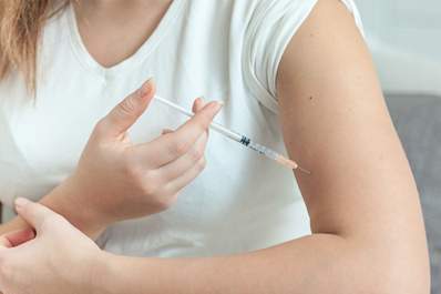 Young woman administering a self injection in her arm.