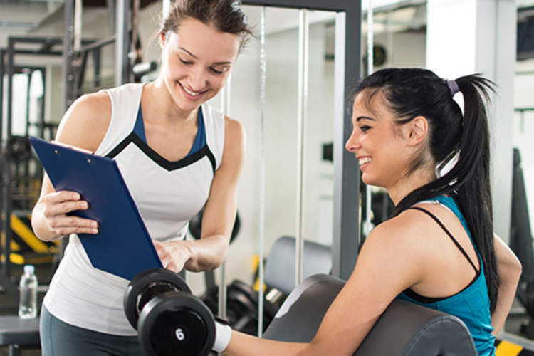 Trainer showing happy young woman good results in gym image.