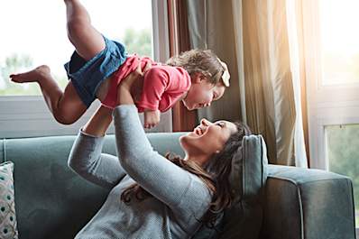 Mother playing with young daughter lifting her up and laughing.