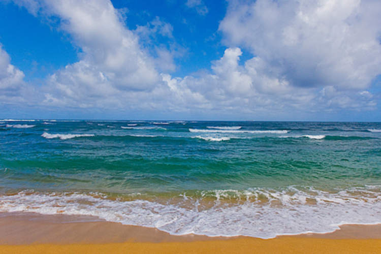 Waves crashing on the beach under a sky filled with clouds.