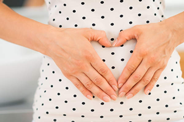 Woman holding hands in heart shape on her belly.