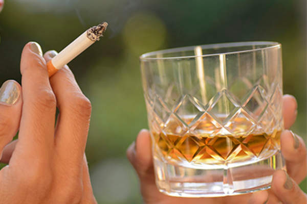 Woman smoking a cigarette and drinking a glass of whiskey.