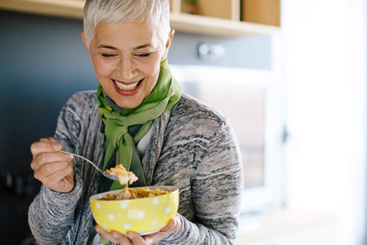 Smiling senior woman eating a bowl of cereal.