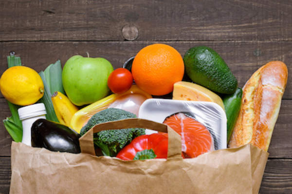 Grocery bag spilling out healthy foods onto table.
