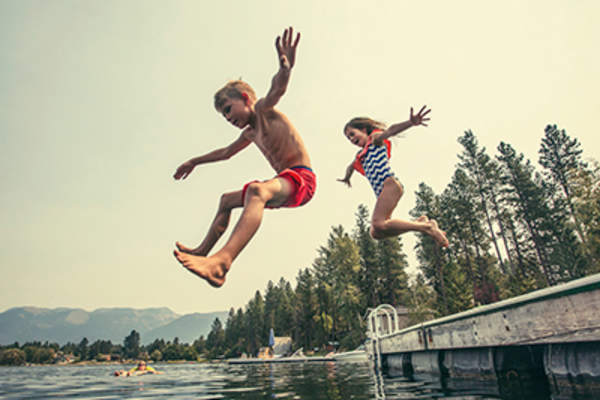 Kids jumping off the dock into a lake .