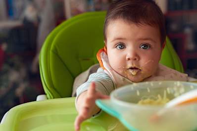 Baby sitting in high chair being fed.