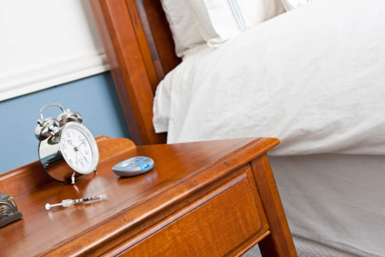 Syringe and glucose meter with alarm clock on nightstand.
