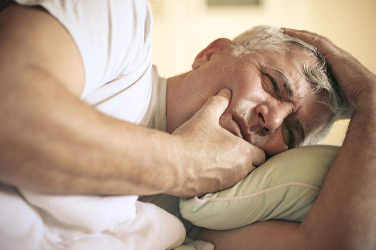 Senior man lying in bed having dental pain.