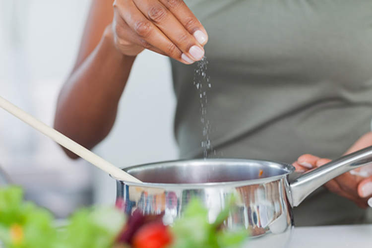 Woman adding salt to pot cooking on stove.