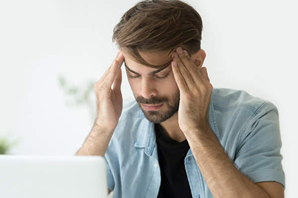 Man rubbing temples at laptop.