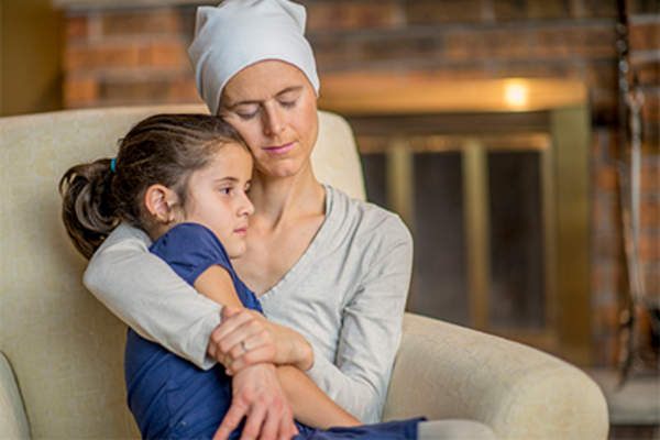 Female cancer patient hugging her young daughter at home.
