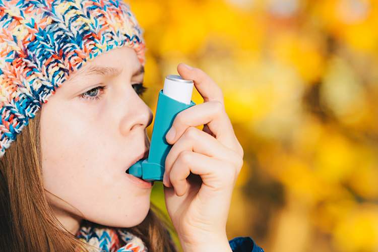 Girl using asthma inhaler in park in autumn.