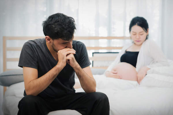 Pregnant couple on bed in disagreement.