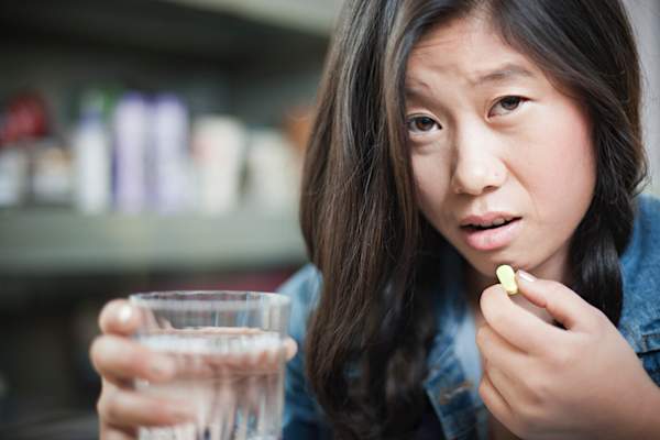 Unhappy Asian teenage girl holding pill and glass of water