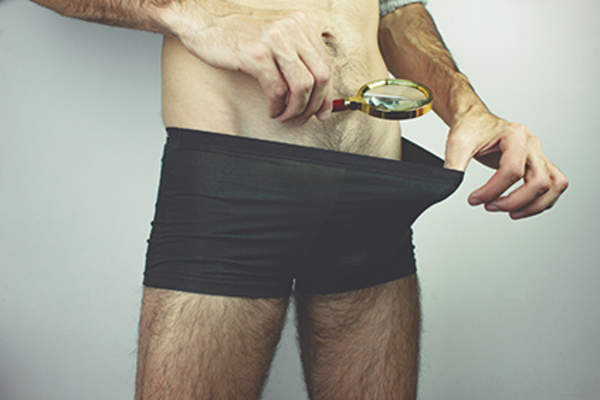 Man looking inside his underwear with a magnifying glass.