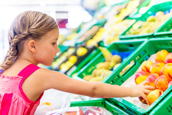 Young girl selecting a peach at the grocery store.