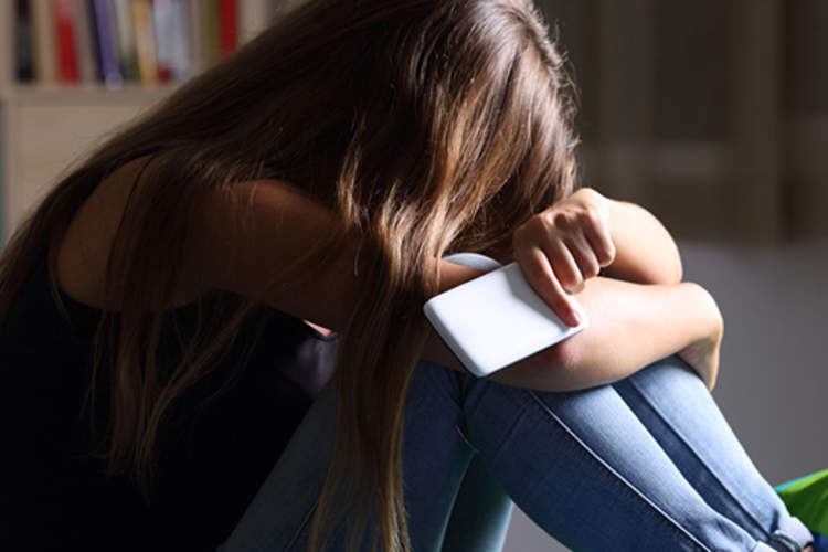 Depressed teen girl holding phone with head down.