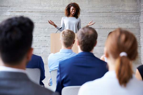 Young woman speaks to an audience at a conference.