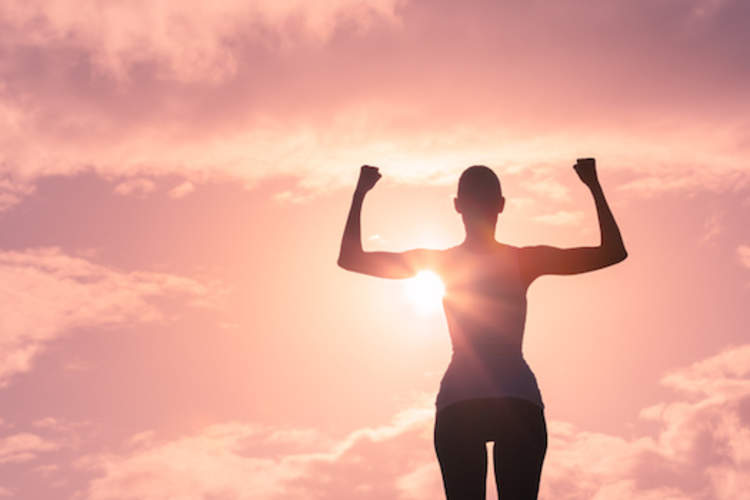 Person raising their arms in sign of strength with sun shining behind them.
