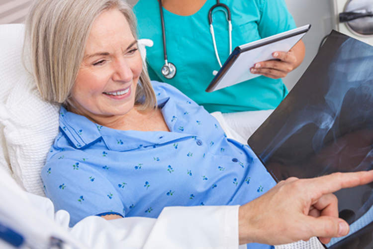 Doctor showing happy senior woman with hip replacement x-ray image.