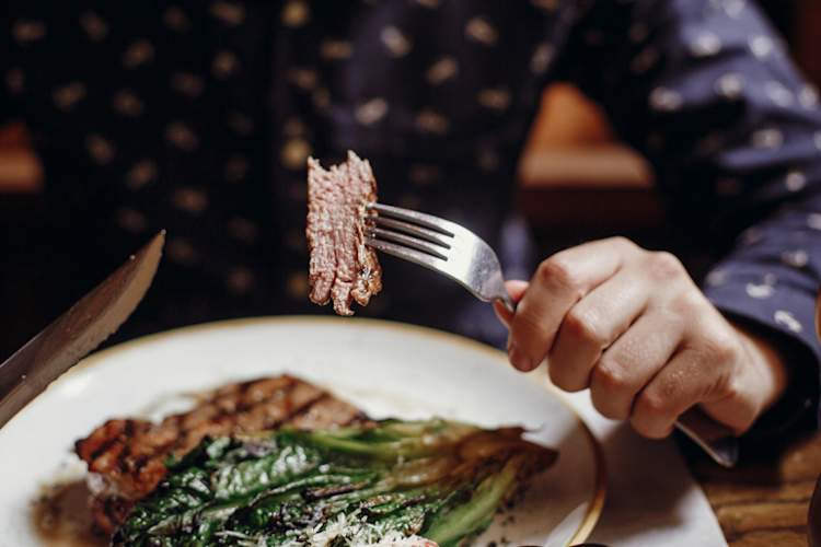 Hands holding fork and knife and eating steak