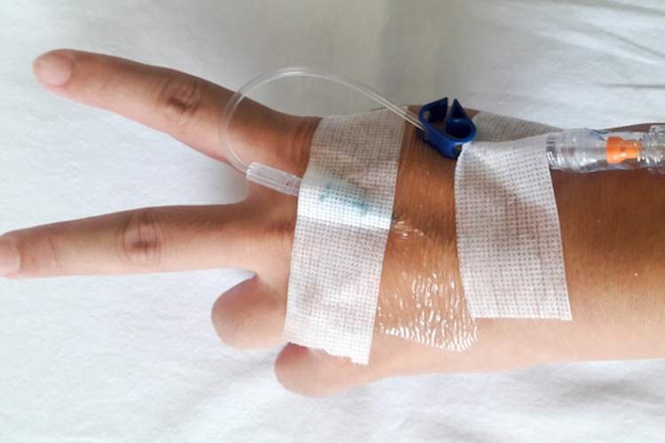 Patient hand with V sign and the tube of normal saline infusion on white cloth background.