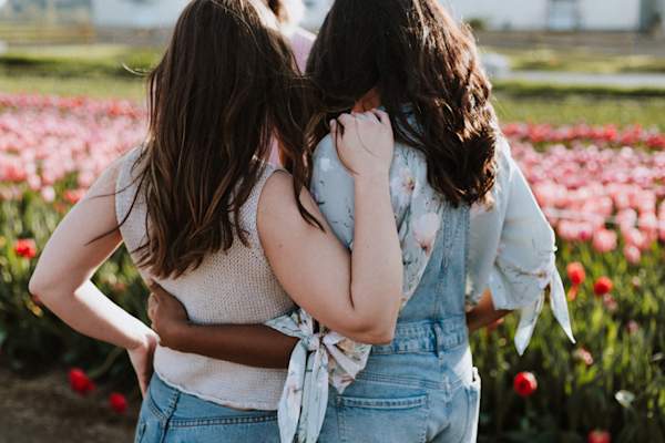 two women hugging each other, from behind