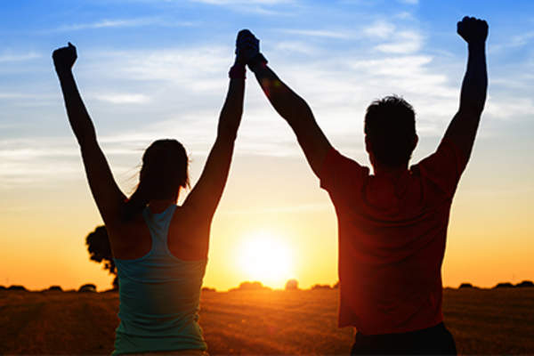 Couple with arms raised with the sunset.