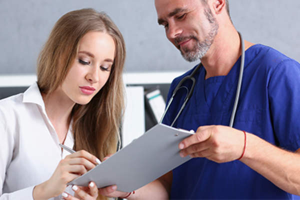 Woman signing a medical form with doctor.