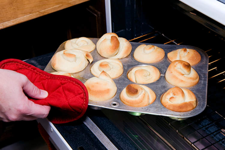 Woman taking rolls out of the oven.