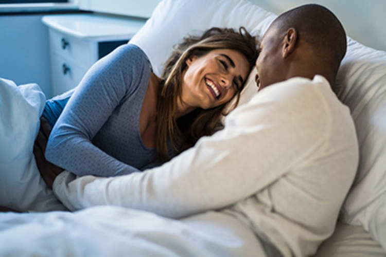 Couple smiling at each other in bed.