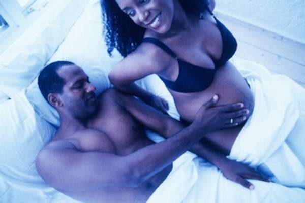 Toned high angle view of a man touching his pregnant wife's stomach in bed.